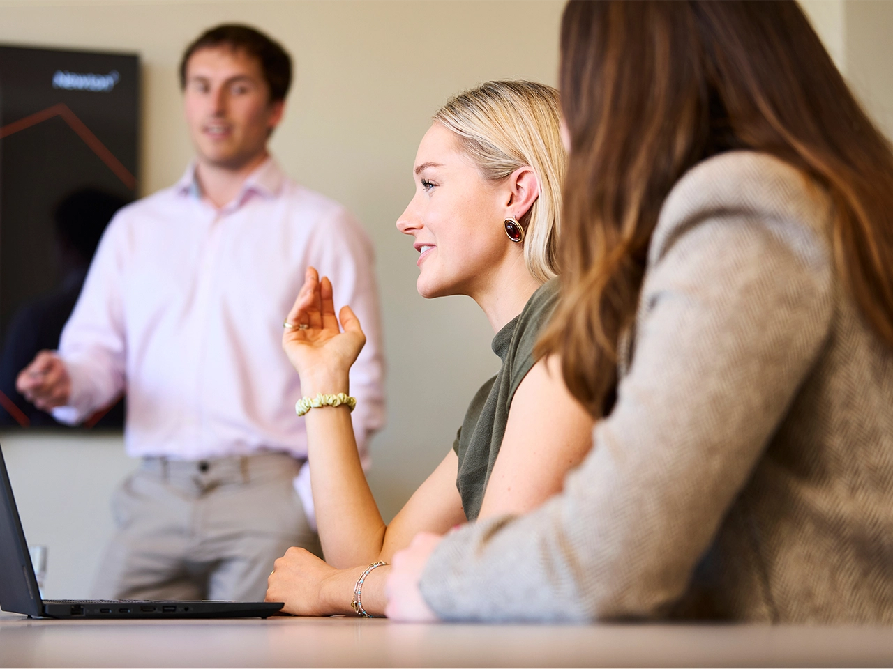 A business meeting with a man presenting in front of a screen, while two women listen.